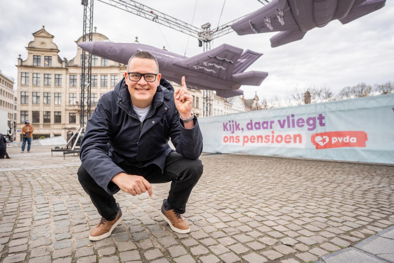 Raoul Hedebouw gehurkt voor de 3 opblaasbare F-35's en het spandoek 'Kijk, daar vliegt ons pensioen’